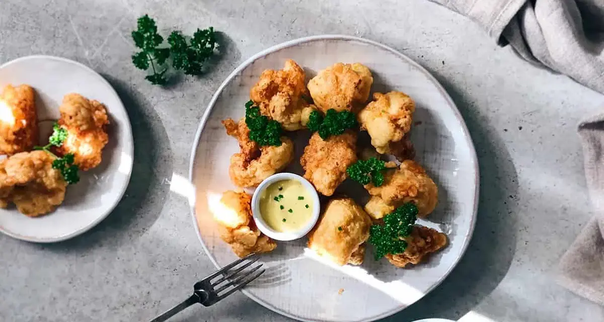 Crujientes trozos de coliflor rebozada, servidos con una cremosa salsa y decorados con perejil fresco. ¡Un aperitivo delicioso!