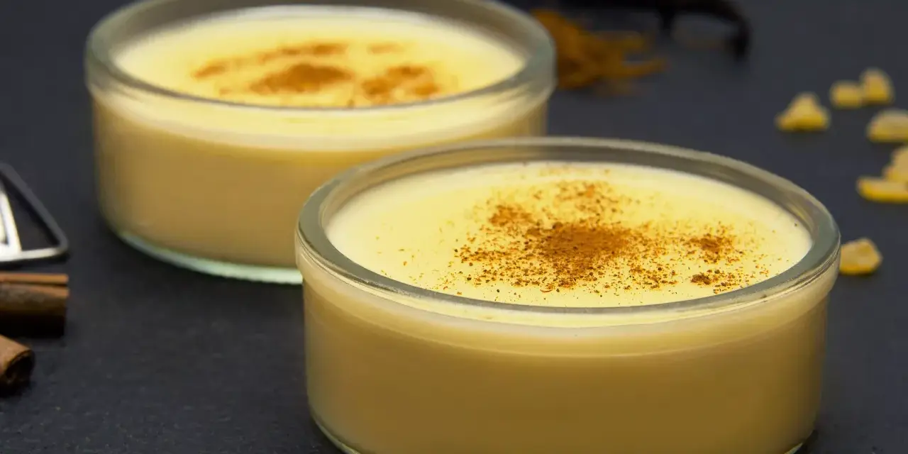 Dos cuencos de natillas caseras, espolvoreadas con canela, junto a palitos de canela y vainilla.
