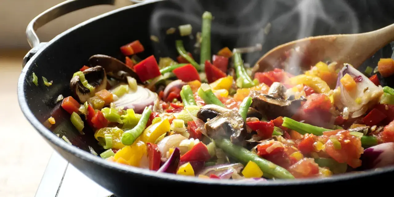 Un delicioso salteado de verduras humeante en un wok, con pimientos, judías verdes, champiñones y cebolla morada.