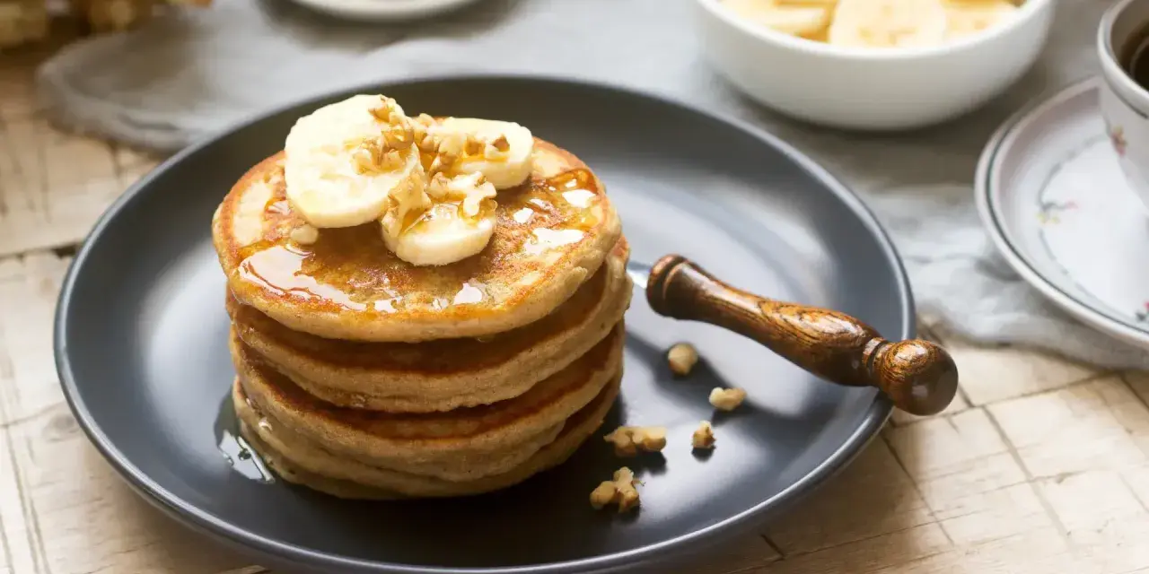 Pila de tortitas americanas con plátano, nueces y sirope. Un desayuno delicioso y nutritivo.