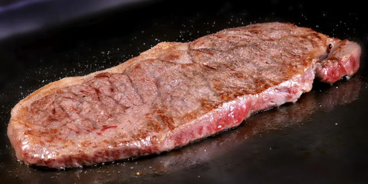 Un jugoso filete de ternera, perfectamente cocinado, chisporrotea en la plancha, listo para ser disfrutado.