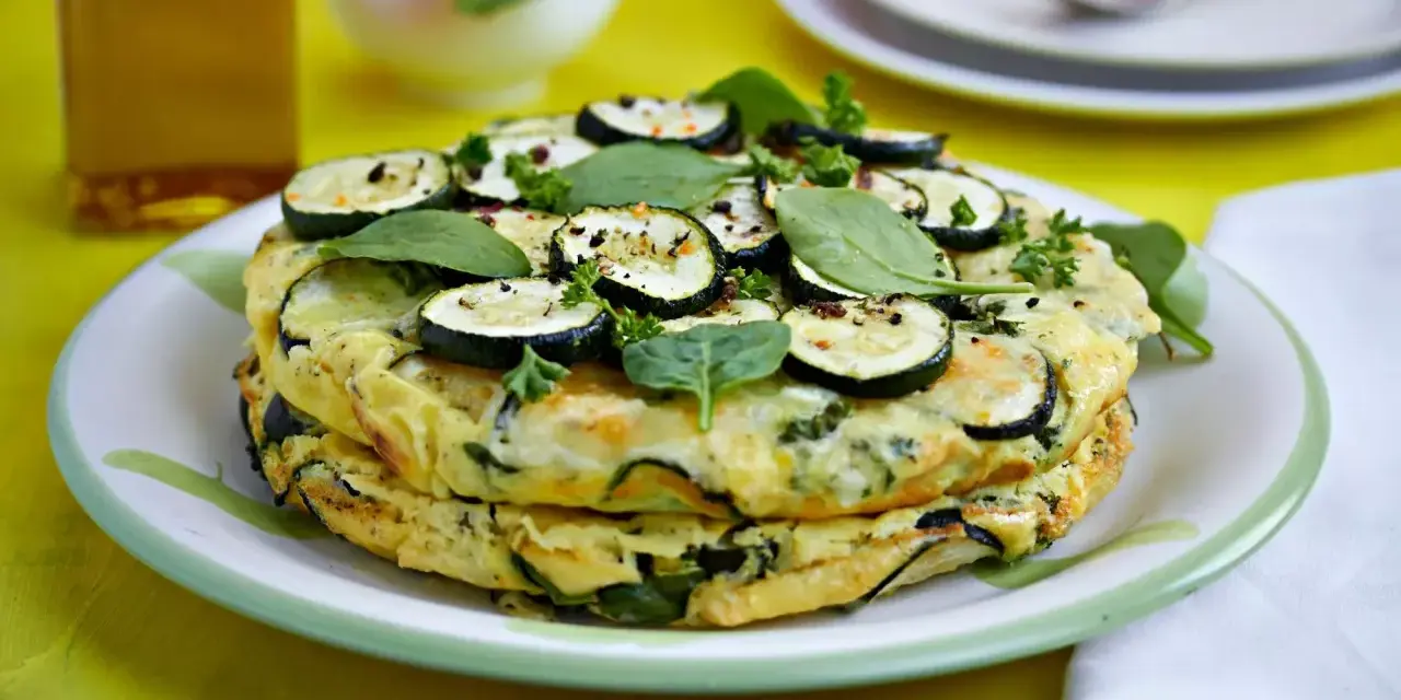 Deliciosa tortilla de calabacín y espinacas, coronada con rodajas de calabacín y hierbas frescas.