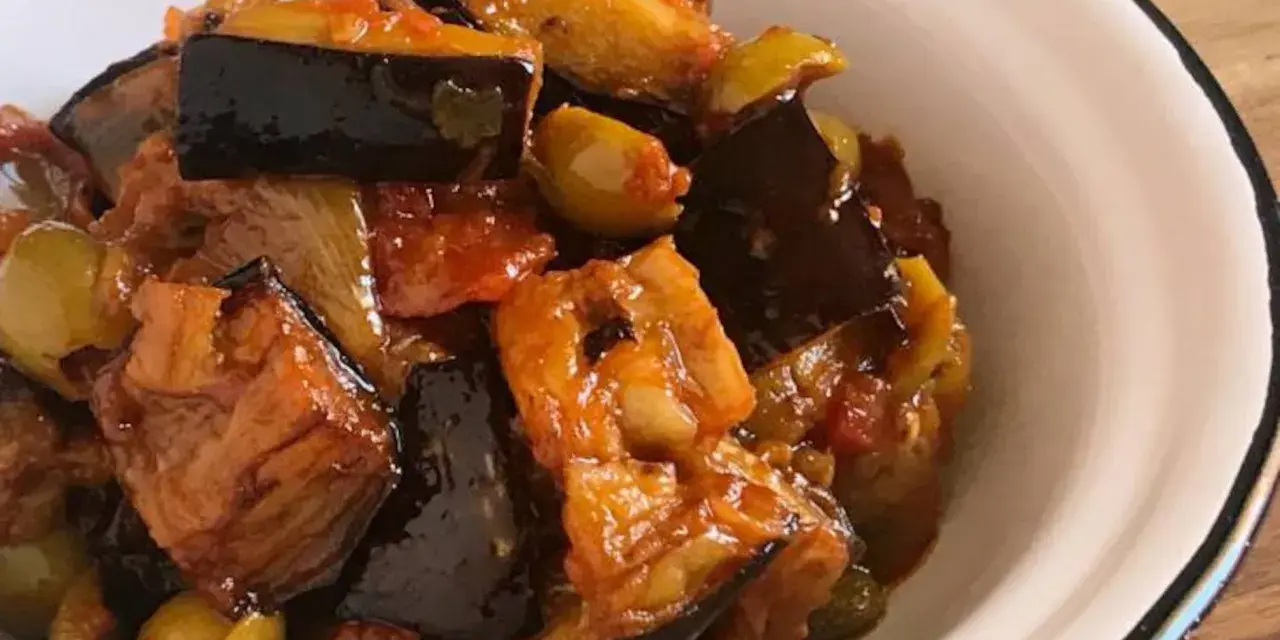 Un plato de caponata siciliana, con berenjenas, aceitunas y tomate, servido en un cuenco blanco.