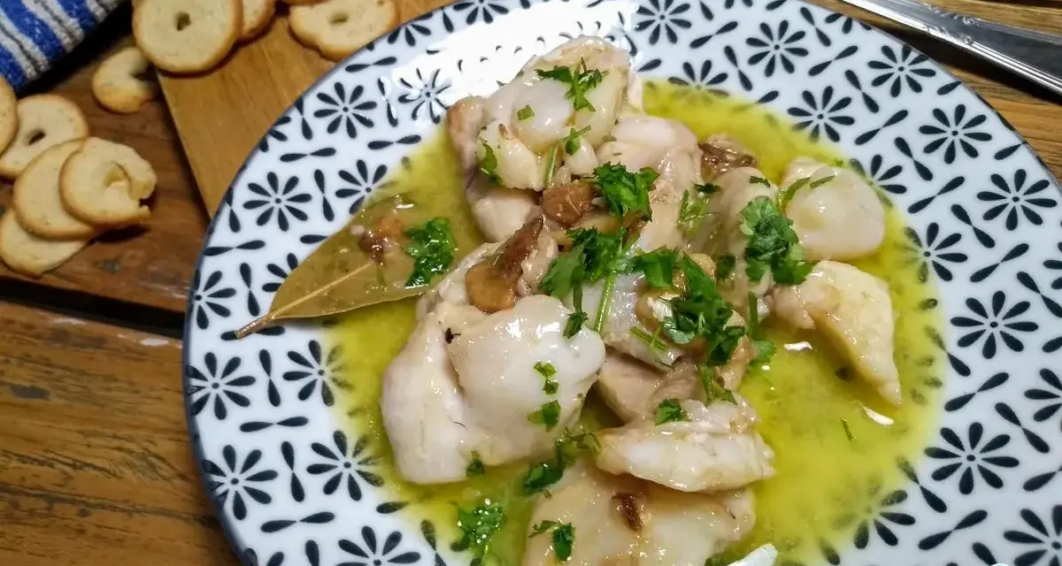 Plato de que son las cocochas de bacalao, tiernas y jugosas, en una salsa amarilla con perejil picado y galletas tostadas al lado.