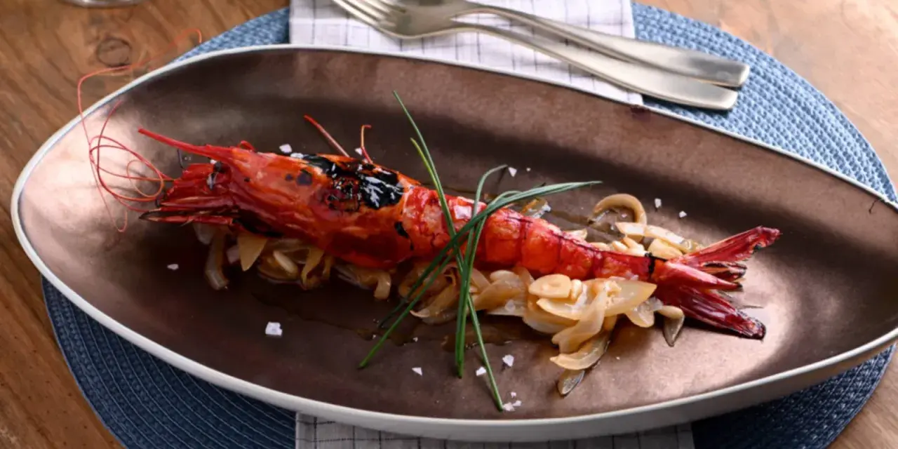 Un langostino rojo a la parrilla, servido sobre cebolla caramelizada y adornado con cebollino. Un plato que evoca la pregunta: ¿qué son los carabineros?