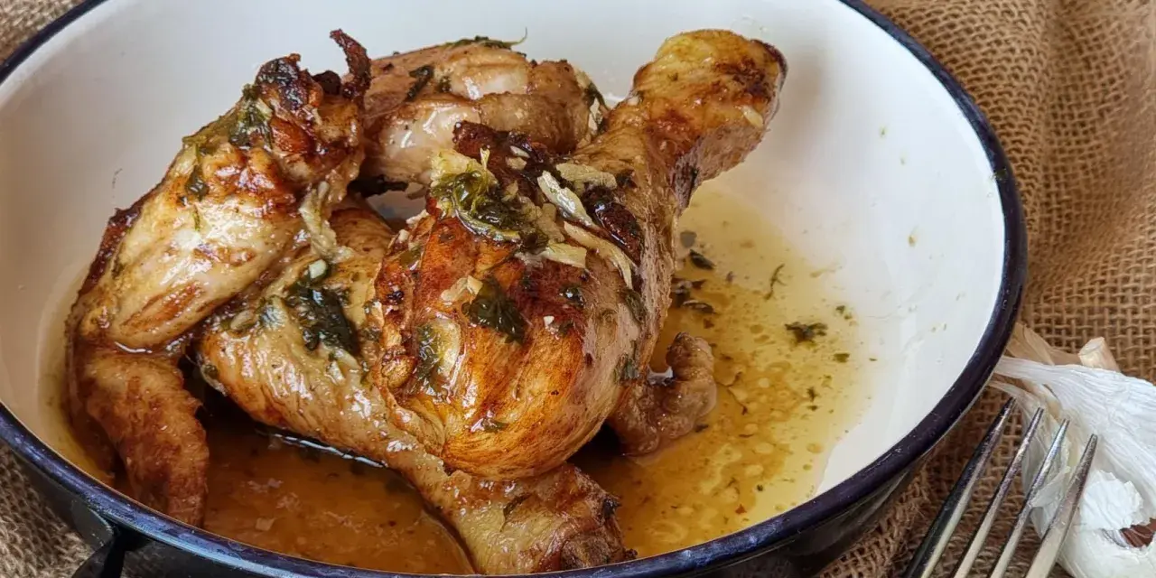 Sabroso pollo al ajillo dorado y jugoso, servido en una cazuela con su jugo y hierbas.