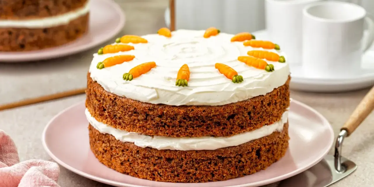 Delicioso bizcocho de zanahoria de dos pisos, cubierto con glaseado blanco y decorado con zanahorias de mazapán.