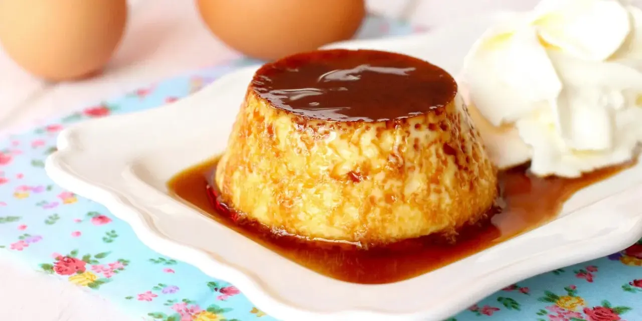 Delicioso flan de huevo casero con caramelo líquido y una porción de nata montada. Huevos frescos al fondo.