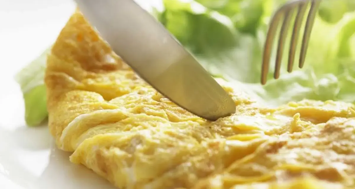 Un cuchillo corta una dorada tortilla francesa servida con hojas de lechuga fresca.