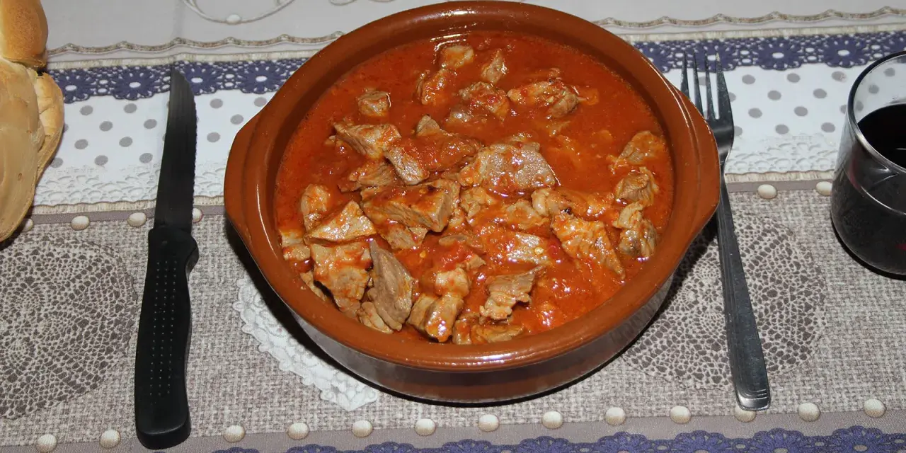 Un cuenco de barro rebosante de magro con tomate, listo para ser disfrutado con pan y vino tinto.