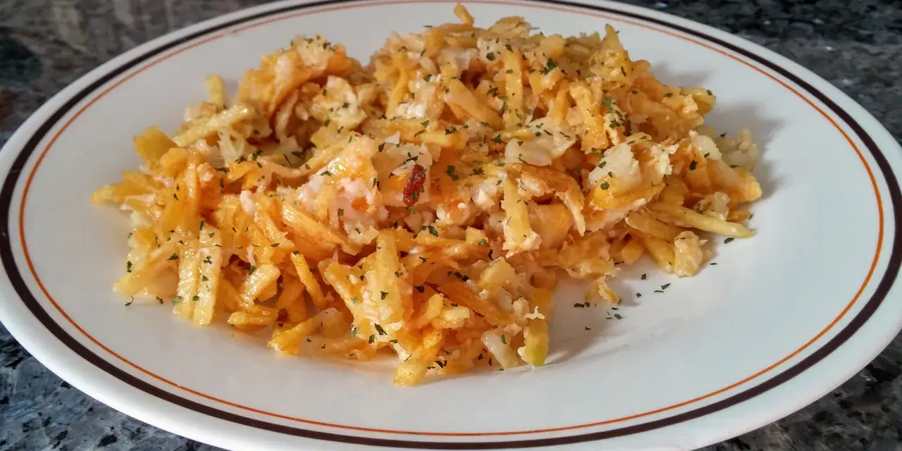 Bacalao dorado desmenuzado con patatas fritas finas y perejil picado, servido en un plato blanco con borde marrón y naranja.