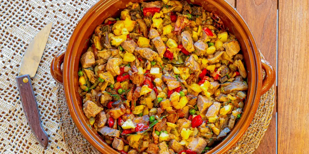 Un generoso plato de frito mallorquín, con trozos de carne, patatas, pimientos y guisantes, servido en una cazuela de barro.