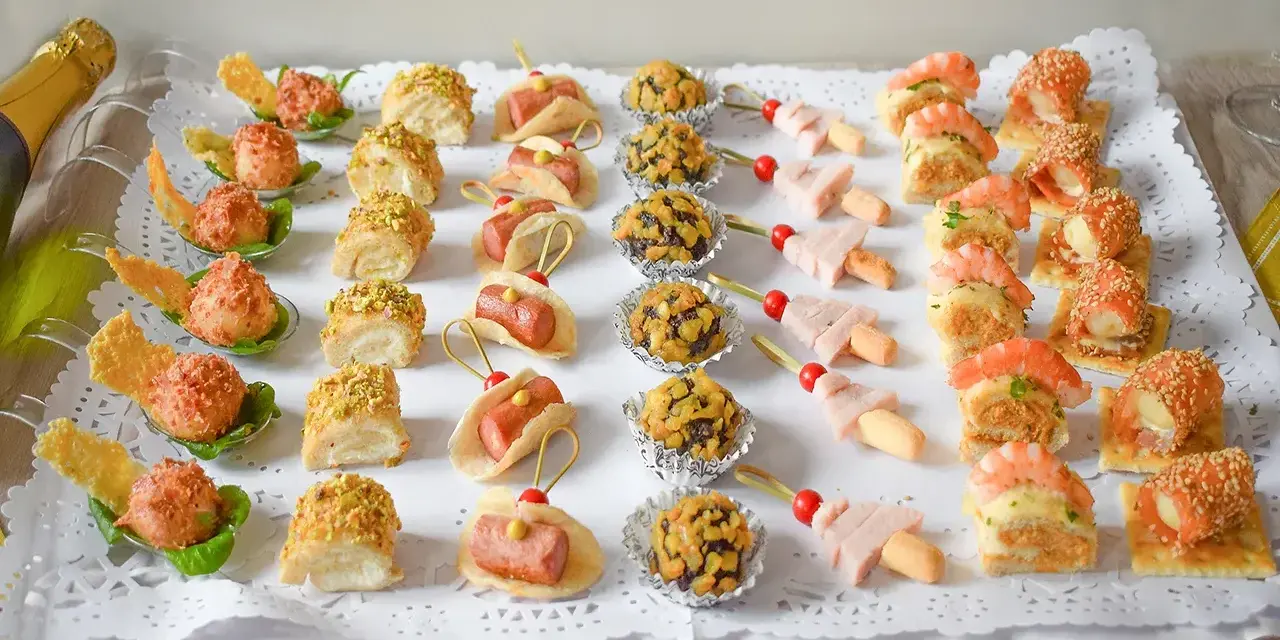 Bandeja con aperitivos navideños originales: mini tacos, bolitas de pistacho, brochetas de jamón y gambas, y rollitos de salmón.