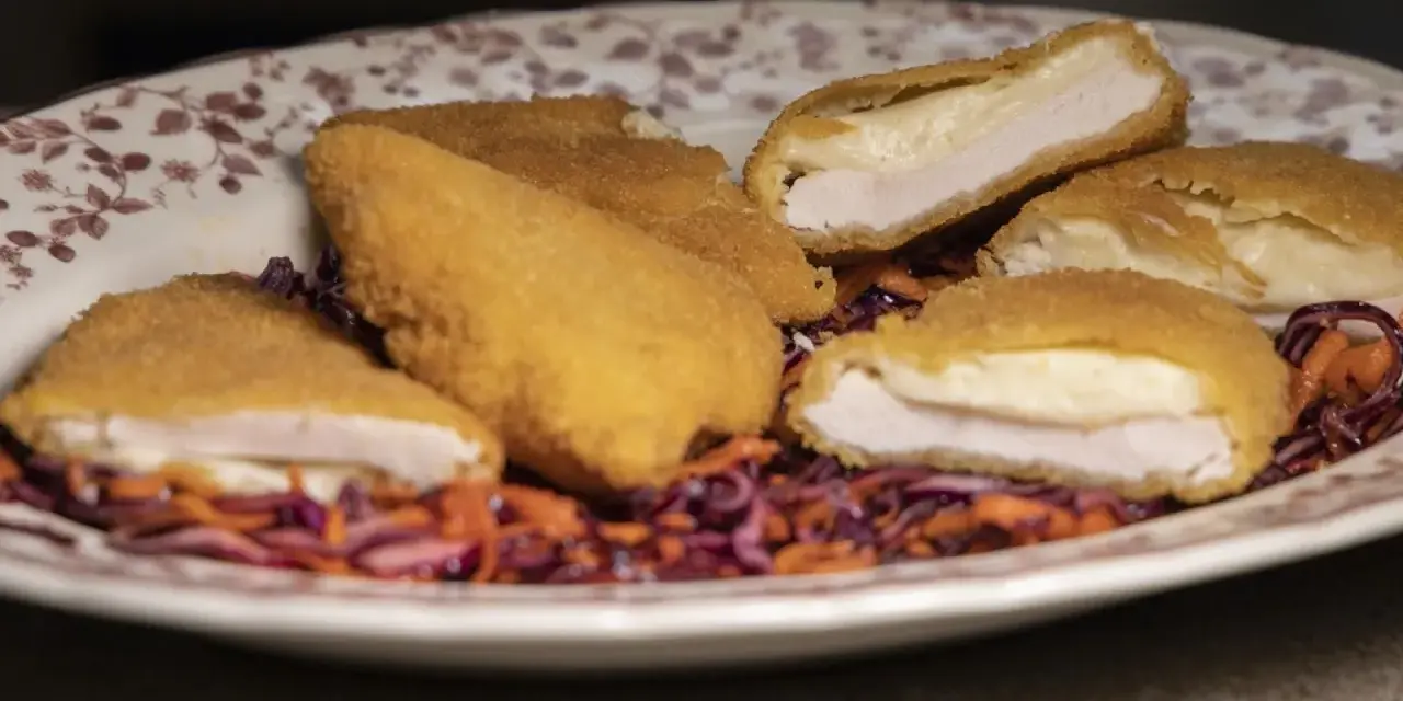 Pechuga villaroy dorada y crujiente, rellena de queso fundido, servida sobre una ensalada de col morada y zanahoria.