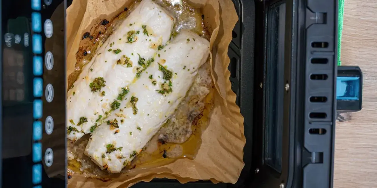 Dos filetes de merluza con hierbas cocinándose en papel de horno dentro de una freidora de aire.
