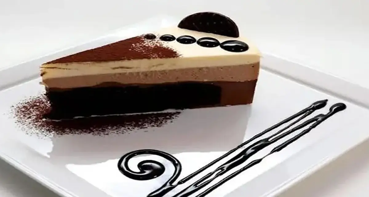 Deliciosa tarta de tres chocolates, con capas de mousse de chocolate blanco, con leche y negro, decorada con cacao y un toque de galleta.