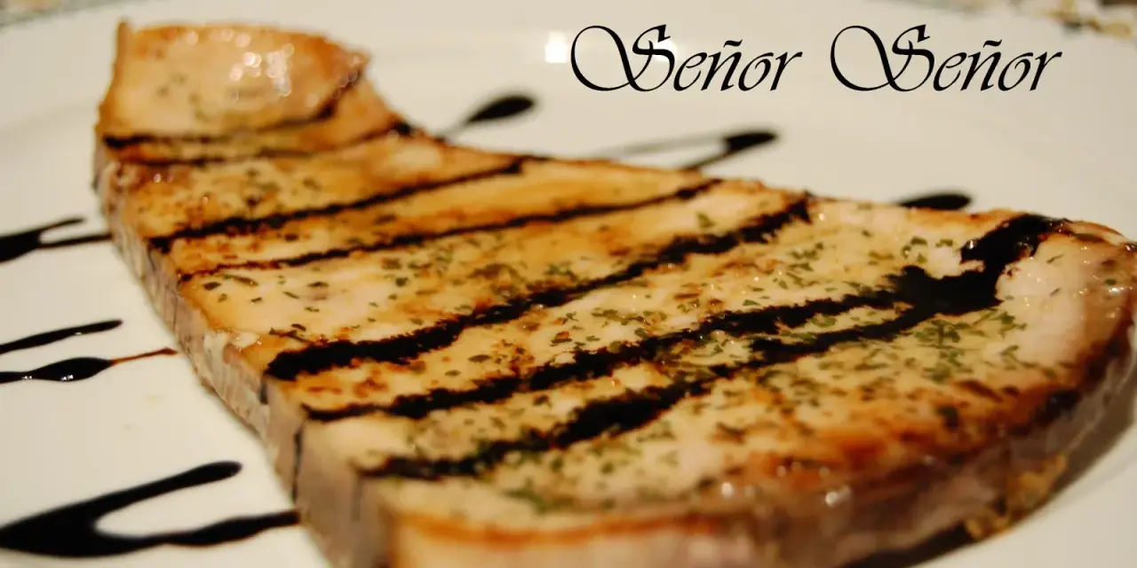 Un delicioso emperador a la plancha, con marcas de parrilla y un toque de hierbas, bañado en salsa oscura. ¡Un manjar digno de un Señor!