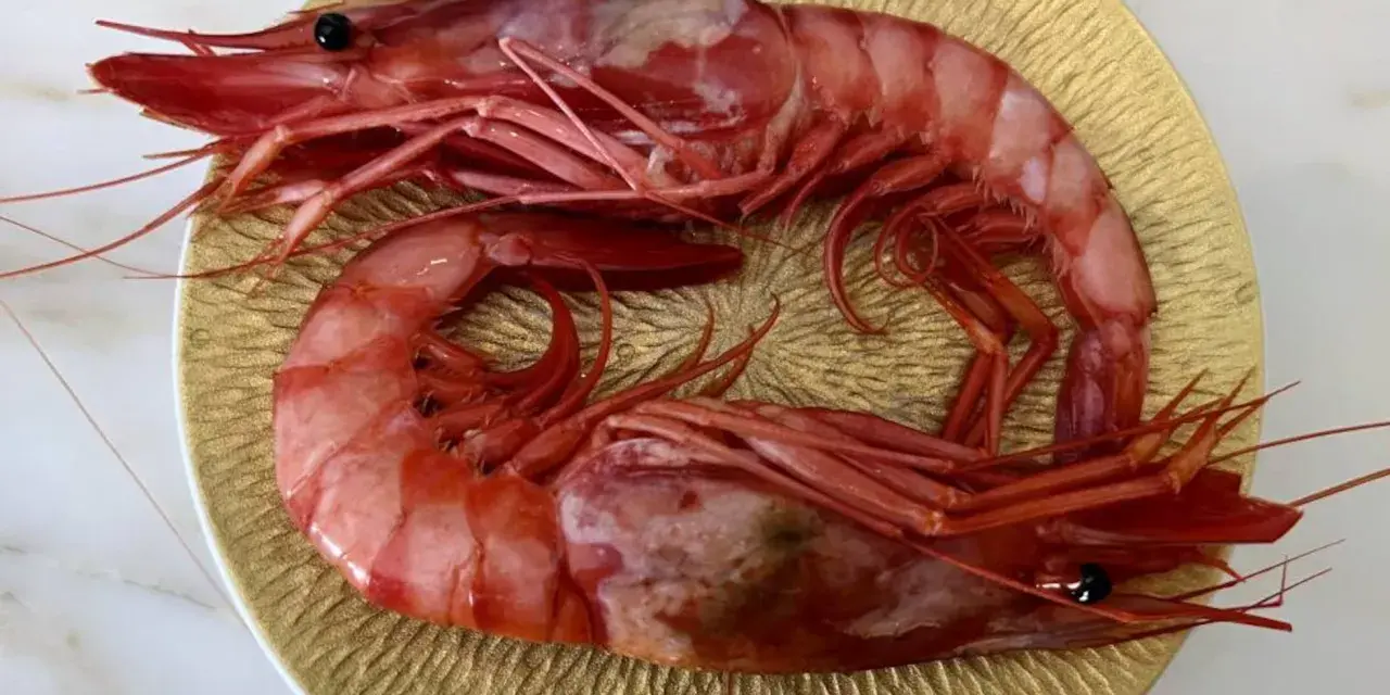 Dos gambas rojas, de distintos tipos, descansan sobre un plato dorado.