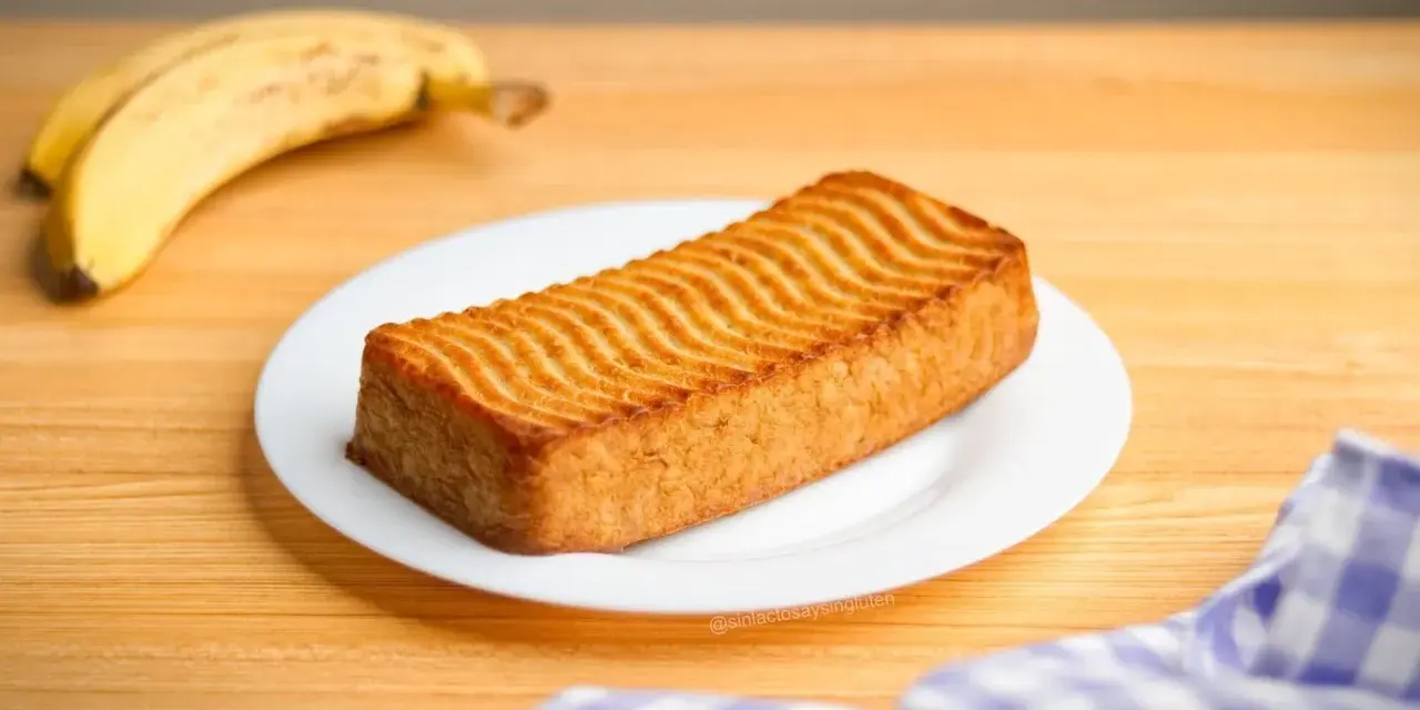 Un delicioso bizcocho de plátano con un patrón ondulado dorado en la parte superior, acompañado de plátanos maduros.