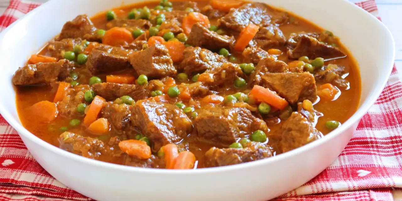 Ternera a la jardinera en un cuenco blanco, con trozos de carne tierna, zanahorias y guisantes en una salsa sabrosa.