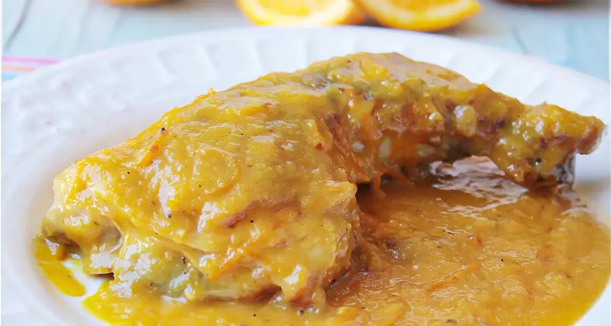Delicioso pollo a la naranja, bañado en una salsa dorada y jugosa, con gajos de naranja frescos al fondo.