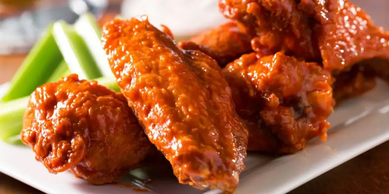 Alitas de pollo en freidora de aire, cubiertas de salsa picante, servidas con bastones de apio crujientes.