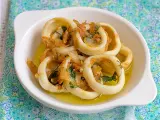 Calamares encebollados en un plato blanco, con cebolla caramelizada y perejil, sobre un mantel azul y verde.