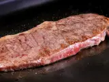 Un jugoso filete de ternera, perfectamente cocinado, chisporrotea en la plancha, listo para ser disfrutado.