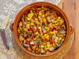 Un generoso plato de frito mallorquín, con trozos de carne, patatas, pimientos y guisantes, servido en una cazuela de barro.