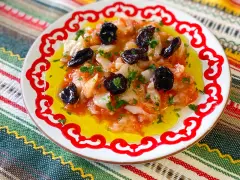 Esqueixada de bacalao con aceitunas negras y perejil, servida en un plato blanco con borde rojo sobre un mantel colorido.