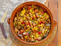 Un generoso plato de frito mallorquín, con trozos de carne, patatas, pimientos y guisantes, servido en una cazuela de barro.