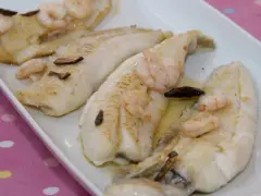 Filetes de gallo a la plancha con gambas y ajo laminado, servidos en una bandeja blanca.