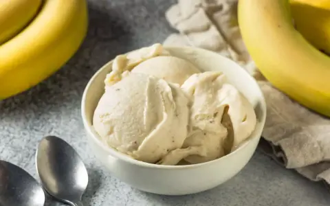Delicioso helado de plátano cremoso en un tazón blanco, con plátanos amarillos frescos al lado.