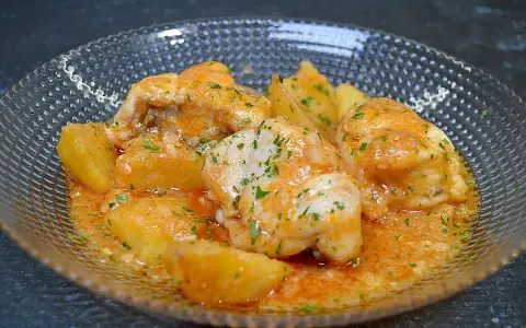 Rape a la marinera con patatas, servido en un cuenco de cristal con salsa naranja y perejil picado.