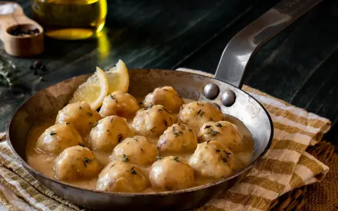 Albondigas de pollo caseras en salsa cremosa, servidas en sartén con limón y hierbas.