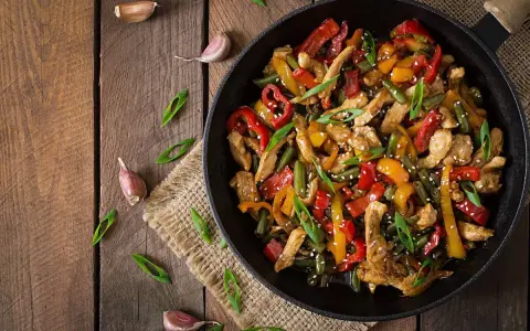 Sabroso wok de pollo con pimientos de colores y judías verdes, espolvoreado con semillas de sésamo y cebolleta.