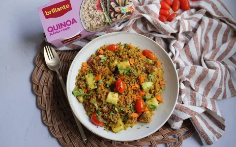 Un plato de quinoa con verduras, incluyendo tomates cherry, calabacín y zanahoria, listo para disfrutar.