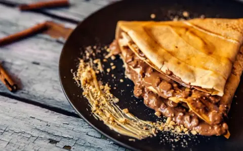Crepe doblada con relleno cremoso de chocolate y trocitos de frutos secos. Ideal para aprender como hacer crepes deliciosos.