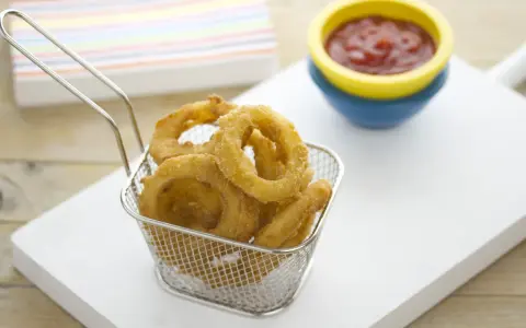 Crujientes aros de cebolla dorados en una cesta metálica, listos para ser sumergidos en kétchup.