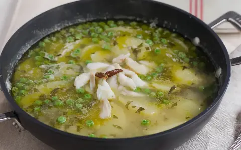 Patatas en salsa verde con trozos de pescado blanco y guisantes, servido en una sartén.