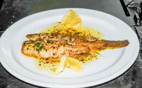 Delicioso lenguado a la meunière, bañado en mantequilla dorada, ajo y perejil, con gajos de limón.