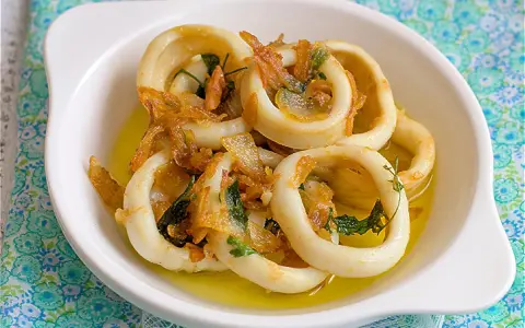 Calamares encebollados en un plato blanco, con cebolla caramelizada y perejil, sobre un mantel azul y verde.