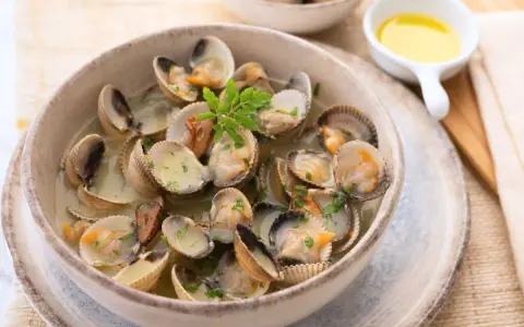 Deliciosos tipos de berberechos cocinados en su jugo, servidos en un cuenco de cerámica con perejil picado.