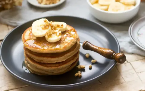 Pila de tortitas americanas con plátano, nueces y sirope. Un desayuno delicioso y nutritivo.