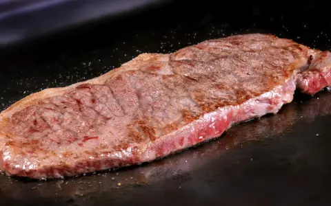Un jugoso filete de ternera, perfectamente cocinado, chisporrotea en la plancha, listo para ser disfrutado.
