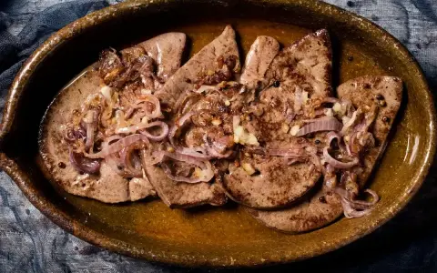 Delicioso hígado encebollado en un plato rústico, con cebolla caramelizada y granos de pimienta.