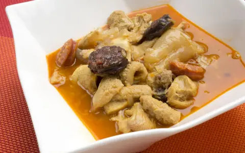 Un plato humeante de callos a la madrileña, con trozos de chorizo y morcilla en una rica salsa.