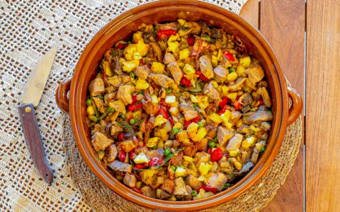 Un generoso plato de frito mallorquín, con trozos de carne, patatas, pimientos y guisantes, servido en una cazuela de barro.