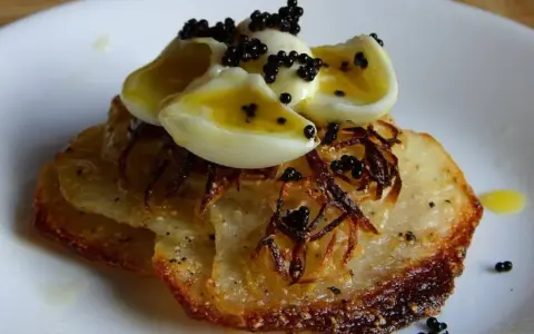 Delicioso aperitivo con patatas crujientes, cebolla frita, huevos de codorniz cocidos y caviar negro.