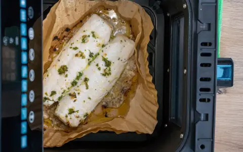 Dos filetes de merluza con hierbas cocinándose en papel de horno dentro de una freidora de aire.